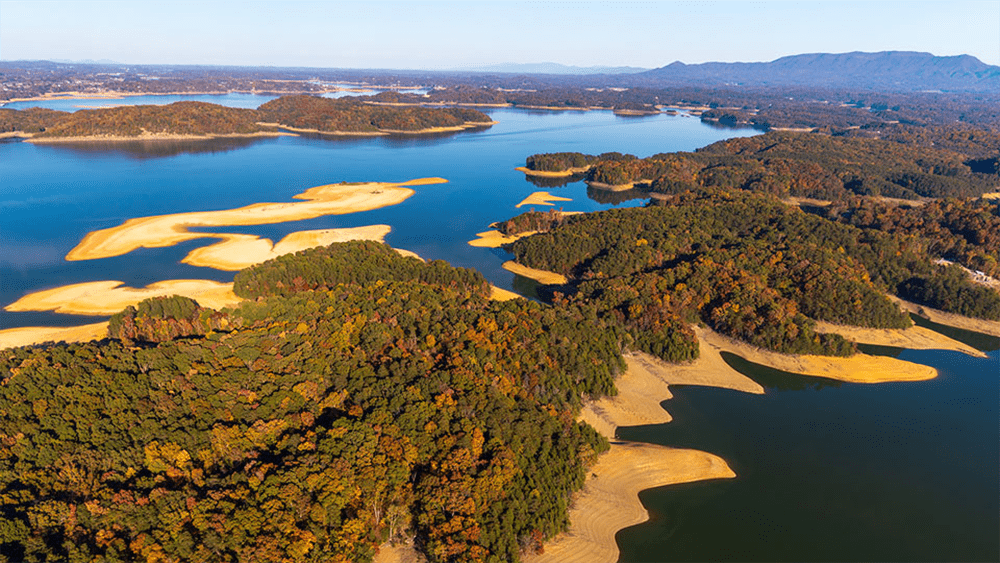 A bird’s-eye view of Douglas Lake in Sevierville, TN as seen from a helicopter, with calm blue water surrounded by green hills and mountains