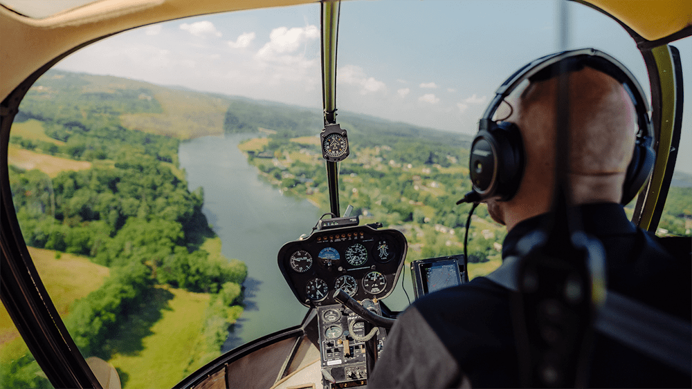 A helicopter pilot wearing a headset and microphone sits at the cockpit controls, ready to guide a scenic Smoky Mountains tour_
