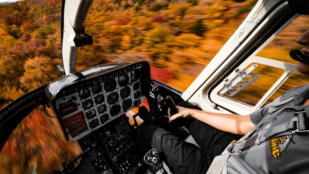 View from inside a tour helicopter, showing the cockpit controls and wide windows revealing the Smoky Mountains landscape outside_